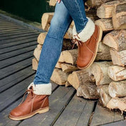 Jeans e stivali in pelle marrone con fodera in pelliccia sintetica, appoggiati su tronchi di legno. Scarpe invernali moda donna.