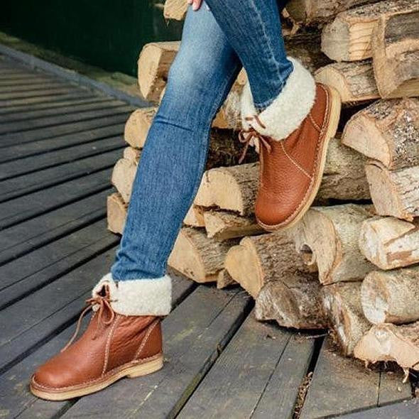 Jeans e stivali in pelle marrone con fodera in pelliccia sintetica, appoggiati su tronchi di legno. Scarpe invernali moda donna.