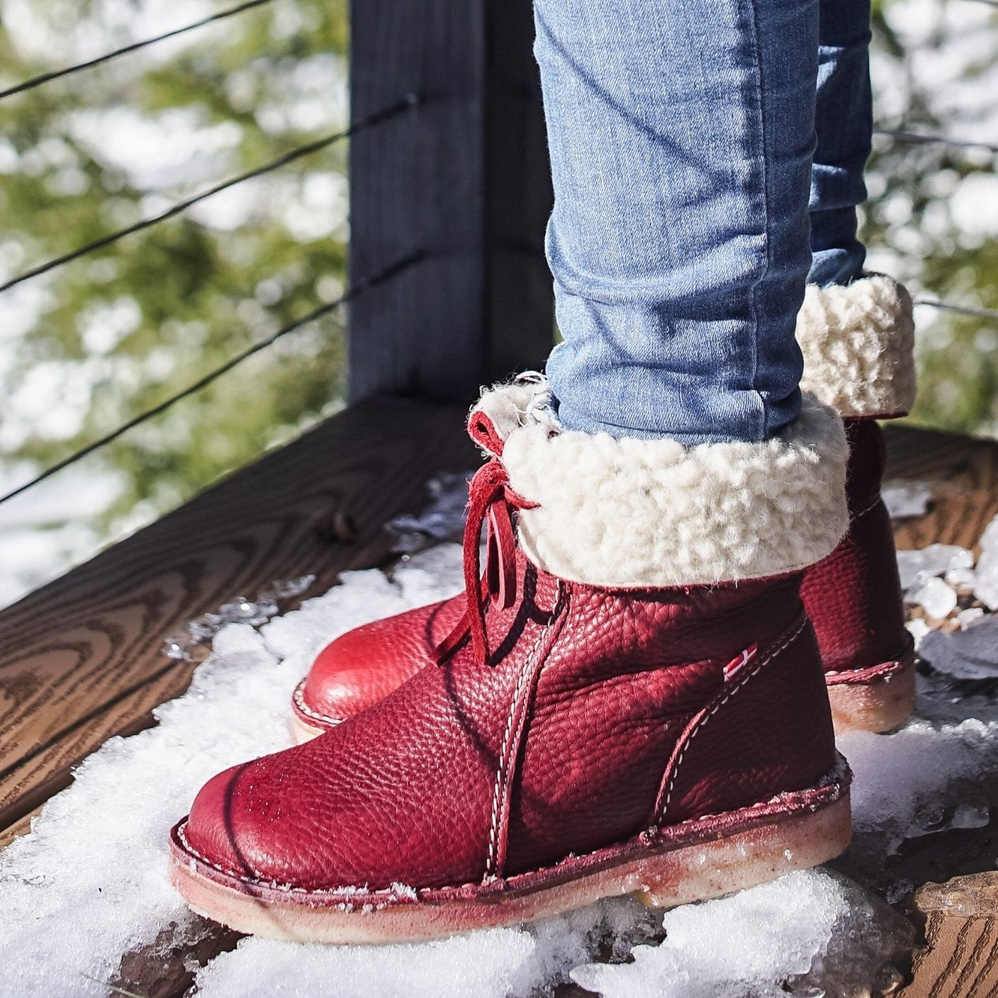 Stivali invernali rossi in pelle con fodera in pelliccia sintetica, indossati su jeans, su terrazza innevata. Scarpe calde e alla moda per l'inverno.