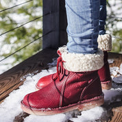 Stivali invernali rossi in pelle con fodera in pelliccia sintetica, indossati su jeans, su terrazza innevata. Scarpe calde e alla moda per l'inverno.