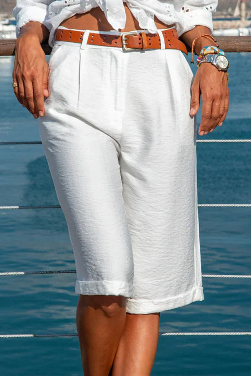 Pantaloncini bermuda bianchi da donna, eleganti e casual, con cintura marrone, perfetti per l'estate. Sfondo marino. Moda estiva femminile.