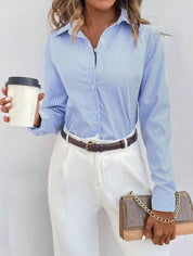 Donna con camicia a righe blu e bianche, pantaloni bianchi eleganti, cintura marrone, borsa a tracolla beige e caffè da asporto. Moda casual chic.