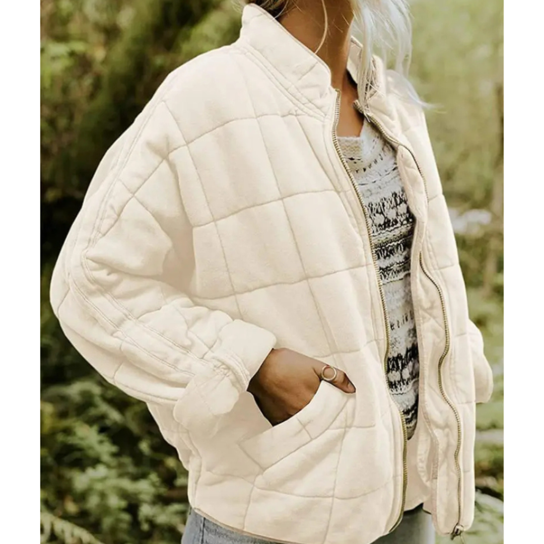 Giacca trapuntata beige da donna, stile casual, con zip frontale e tasche laterali, indossata su maglia a righe. Moda autunnale, abbigliamento femminile.