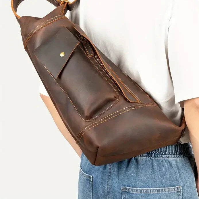 Zaino a tracolla in pelle marrone, design elegante e pratico, indossato su spalla, ideale per viaggi e uso quotidiano. Accessorio moda uomo.