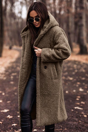 Donna con cappotto teddy marrone, occhiali da sole, pantaloni neri in pelle, in un parco autunnale. Moda invernale, stile casual chic.