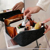Borsa trucco nera aperta con scomparti, contenente cosmetici vari come rossetti, pennelli e flaconi. Mani femminili organizzano il contenuto.