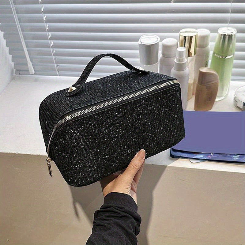Borsa cosmetica nera glitterata con cerniera, manico superiore, su mensola con flaconi e specchio. Elegante e pratica per trucco e accessori.