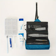 Borsa da toilette da viaggio blu appesa aperta con scomparti, contenente articoli da bagno. Include asciugamano, spazzolino, dentifricio, pettine.