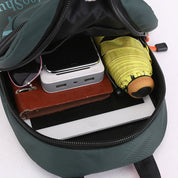 Zaino verde aperto con tablet, power bank, occhiali da sole, portafoglio in pelle e ombrello giallo. Accessori viaggio, tecnologia, organizzazione.