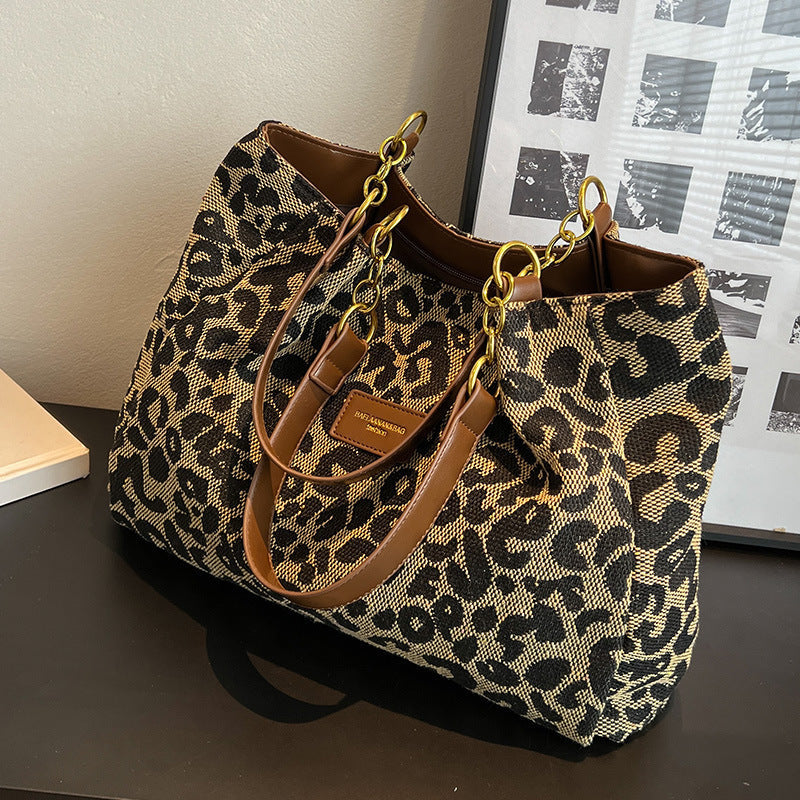 Borsa a tracolla leopardata con manici in pelle marrone e catene dorate, posizionata su un tavolo nero. Accessorio moda elegante e trendy.