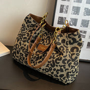 Borsa a tracolla leopardata con manici in pelle marrone e catene dorate, posizionata su un tavolo nero. Accessorio moda elegante e trendy.