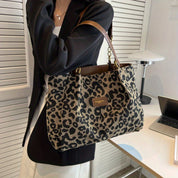 Borsa a spalla leopardata in tessuto, manici in pelle marrone, indossata da una donna in giacca nera. Accessorio moda elegante e trendy.