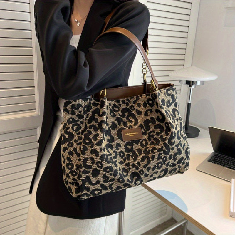 Borsa a spalla leopardata in tessuto, manici in pelle marrone, indossata da una donna in giacca nera. Accessorio moda elegante e trendy.