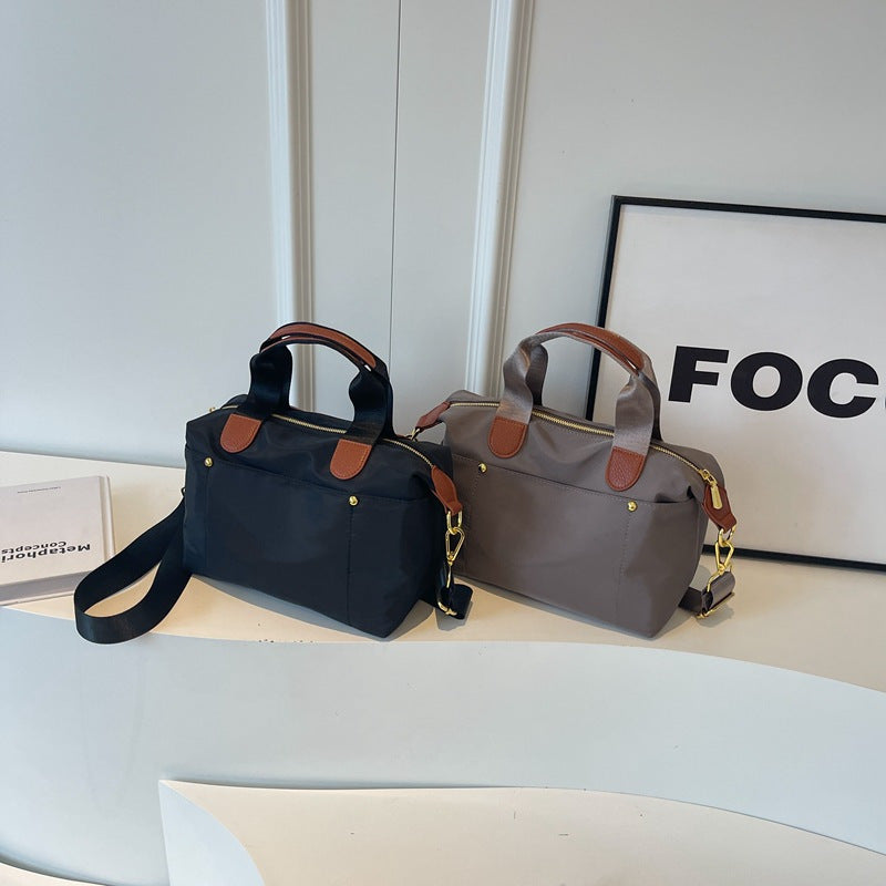 Due borse a mano eleganti in tessuto nero e grigio con dettagli in pelle marrone, esposte su un tavolo bianco. Design moderno e funzionale.