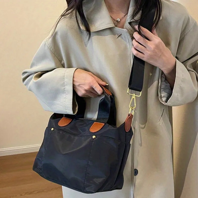 Donna con cappotto beige indossa borsa a tracolla nera in nylon con dettagli in pelle marrone, moda autunno, accessorio elegante e pratico.