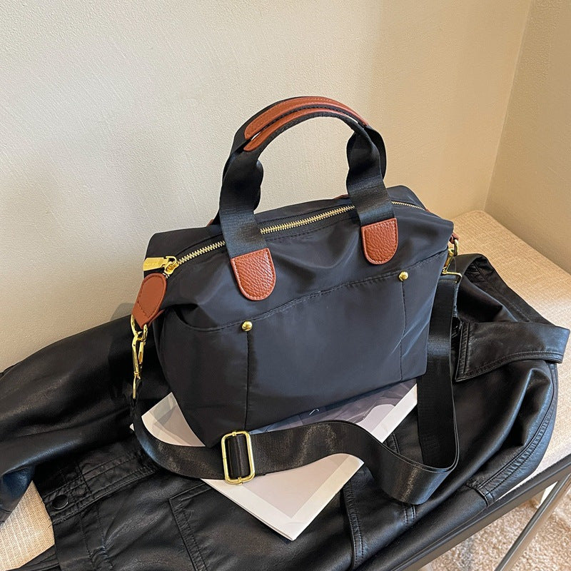 Borsa a tracolla nera in nylon con dettagli in pelle marrone, zip dorata, su giacca di pelle nera. Elegante accessorio moda donna.