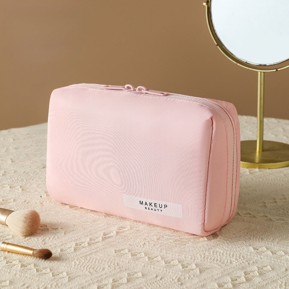 Astuccio trucco rosa su tavolo beige, specchio rotondo, pennelli trucco. Elegante borsa cosmetica, organizer viaggio, accessori bellezza.