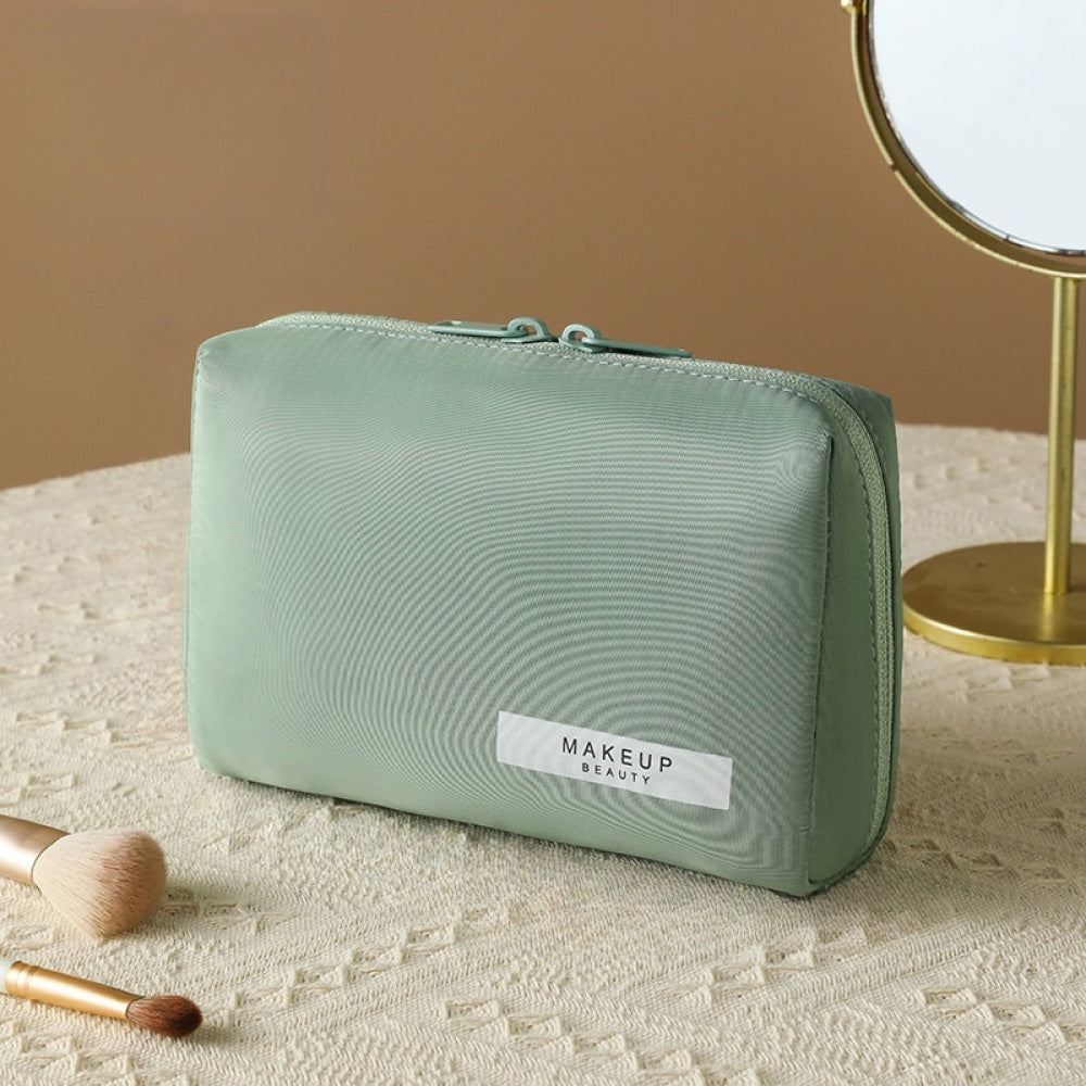 Astuccio trucco verde menta su tavolo beige, con specchio e pennelli. Elegante e pratico, ideale per organizzare cosmetici.