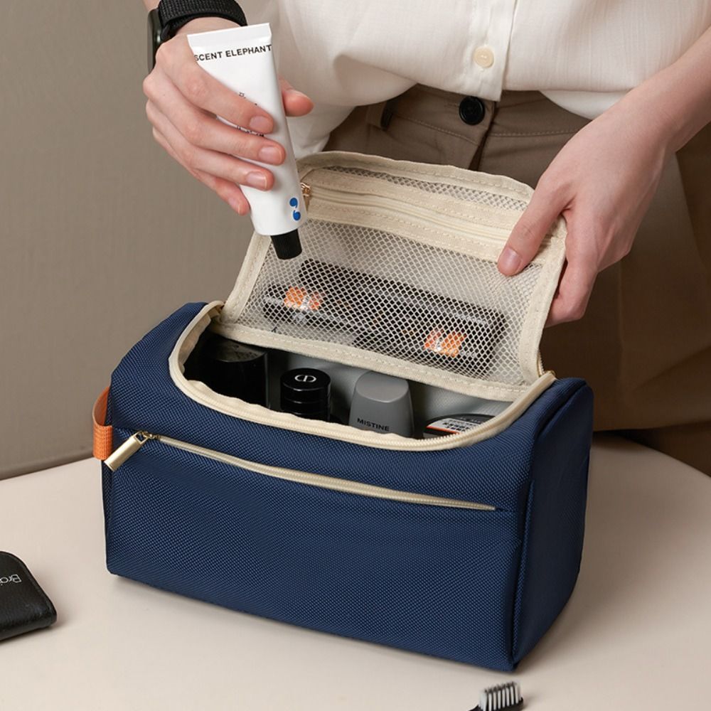 Borsa da toilette blu con cerniera aperta, contenente prodotti per la cura personale. Mani femminili che estraggono un tubetto. Organizzatore da viaggio.
