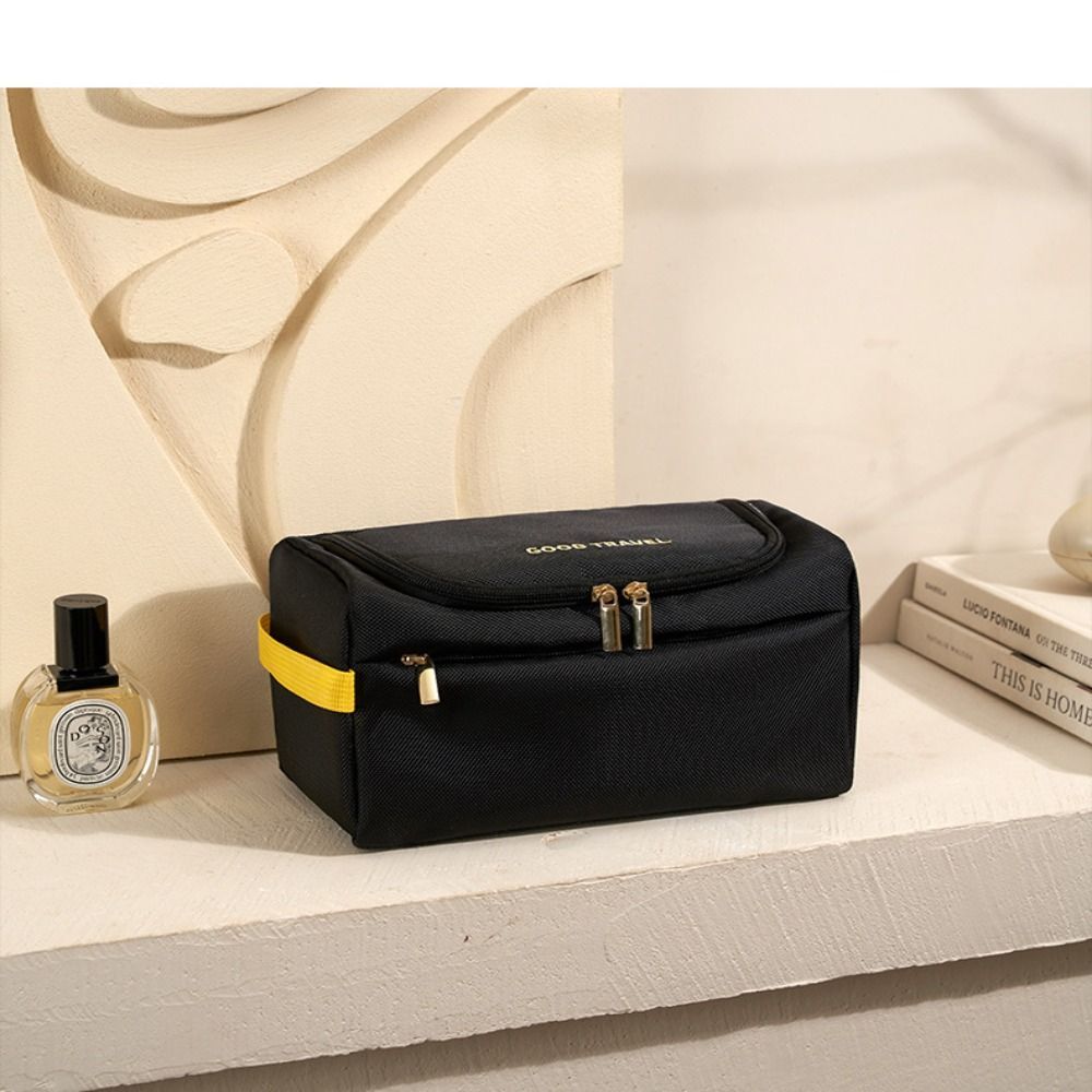 Astuccio da viaggio nero con cerniera, manico giallo, su mensola bianca. Include profumo e libro. Accessorio elegante e pratico per organizzare oggetti personali.