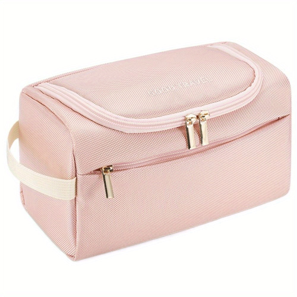 Astuccio da viaggio rosa in tessuto, con doppia cerniera dorata e manico laterale. Ideale per cosmetici e accessori. Design elegante e pratico.
