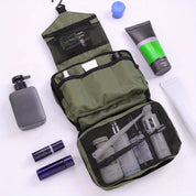 Borsa da toilette verde aperta con scomparti, contenente flaconi e accessori da viaggio. Articoli da bagno e cosmetici disposti intorno.