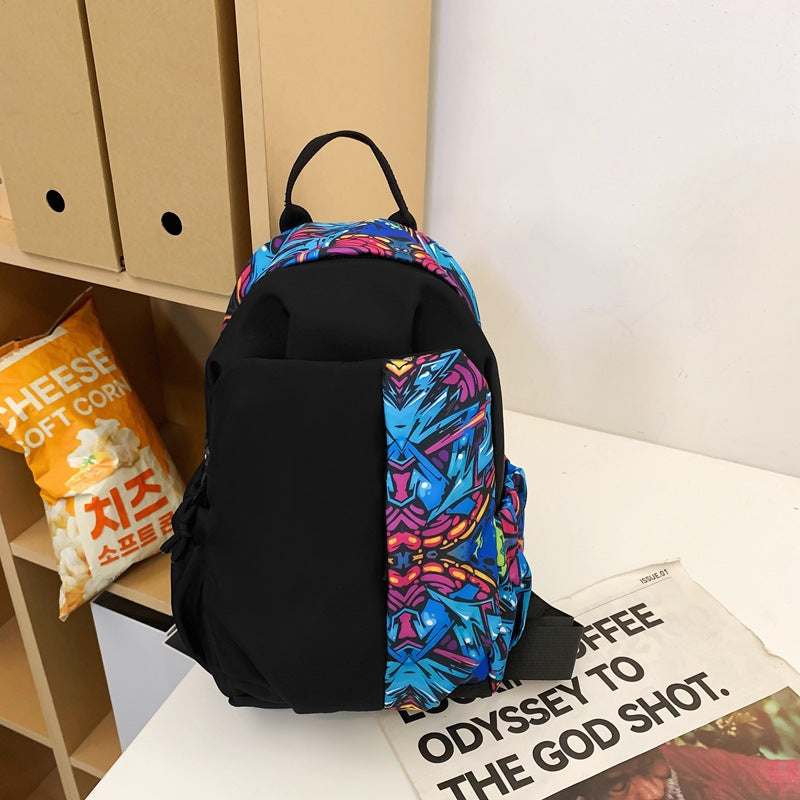 Zaino nero con dettagli colorati blu e rosa su tavolo bianco, accanto a confezione di snack al formaggio. Design moderno e vivace.