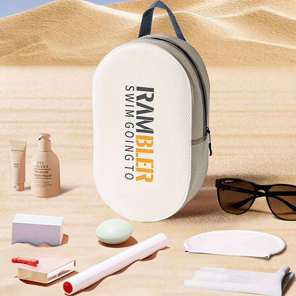 Zaino da spiaggia bianco su sabbia, con scritta "Rambler Swim Going To". Accessori da spiaggia inclusi: occhiali da sole, crema solare, cosmetici.