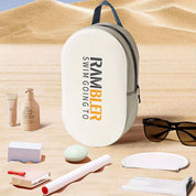 Zaino da spiaggia bianco su sabbia, con scritta "Rambler Swim Going To". Accessori da spiaggia inclusi: occhiali da sole, crema solare, cosmetici.
