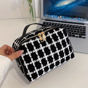 Borsa a mano in tessuto bianco e nero con motivo a scacchi, chiusura a zip dorata, posata su un laptop aperto. Design elegante e moderno.