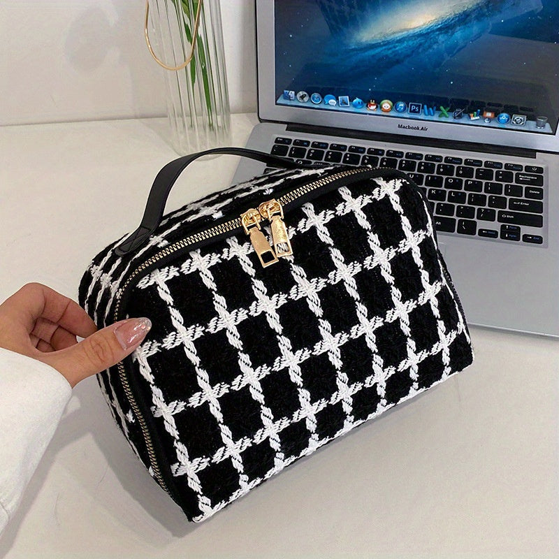Borsa a mano in tessuto bianco e nero con motivo a scacchi, chiusura a zip dorata, posata su un laptop aperto. Design elegante e moderno.