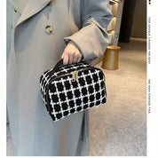 Borsa a mano elegante in tessuto a quadri bianco e nero, chiusura con zip, tenuta da una persona in cappotto grigio. Accessorio moda chic.
