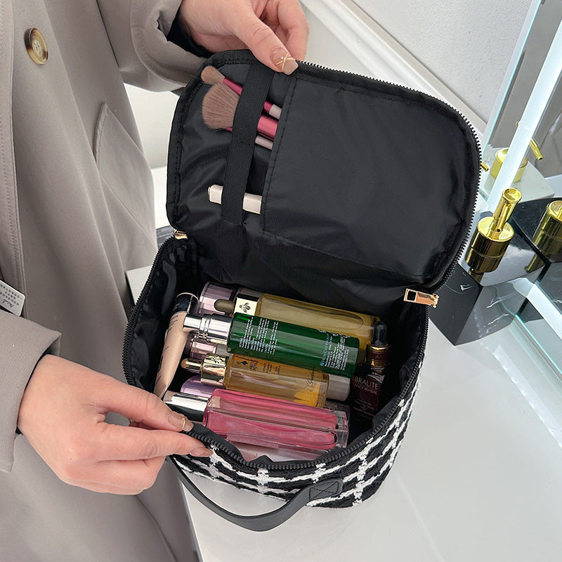 Borsa cosmetica aperta con flaconi di profumo e pennelli trucco, design a quadri, manico nero, su sfondo bagno moderno. Accessori bellezza viaggio.