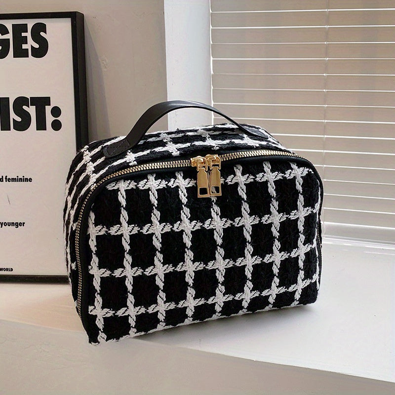 Borsa a mano in tessuto a quadri bianco e nero con manico in pelle nera e chiusura dorata, posizionata su un tavolo vicino a una finestra.