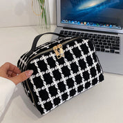 Borsa a mano in tessuto a scacchi bianco e nero con cerniera dorata, posizionata davanti a un MacBook Air su una scrivania moderna.