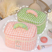 Due beauty case a quadretti, uno verde e uno rosa, con cerniera e manico imbottito, su tavolo da trucco con pennello e specchio.