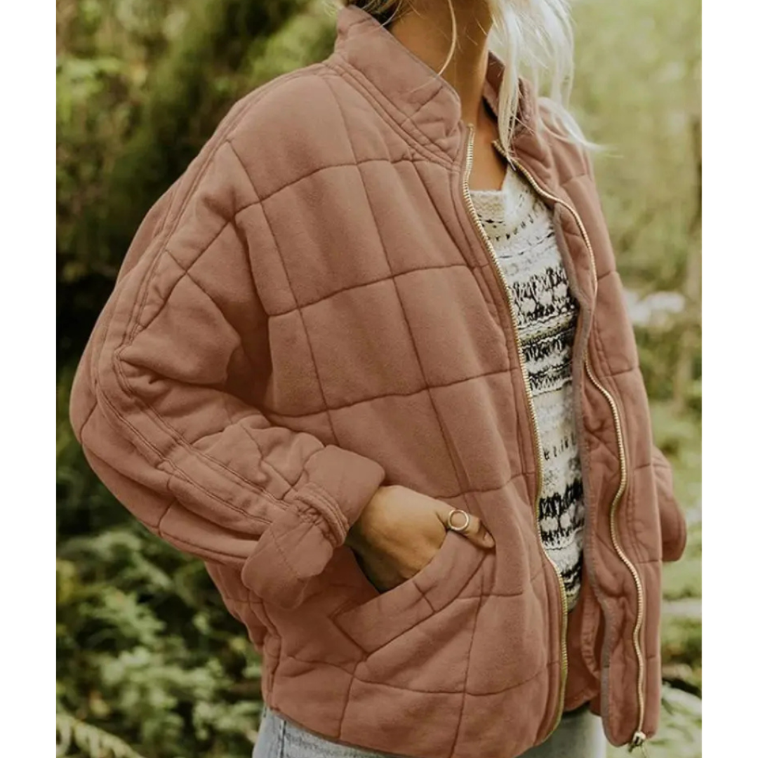 Giacca trapuntata marrone chiaro da donna, stile casual, con zip frontale e tasche, indossata su maglia bianca stampata. Moda autunnale.