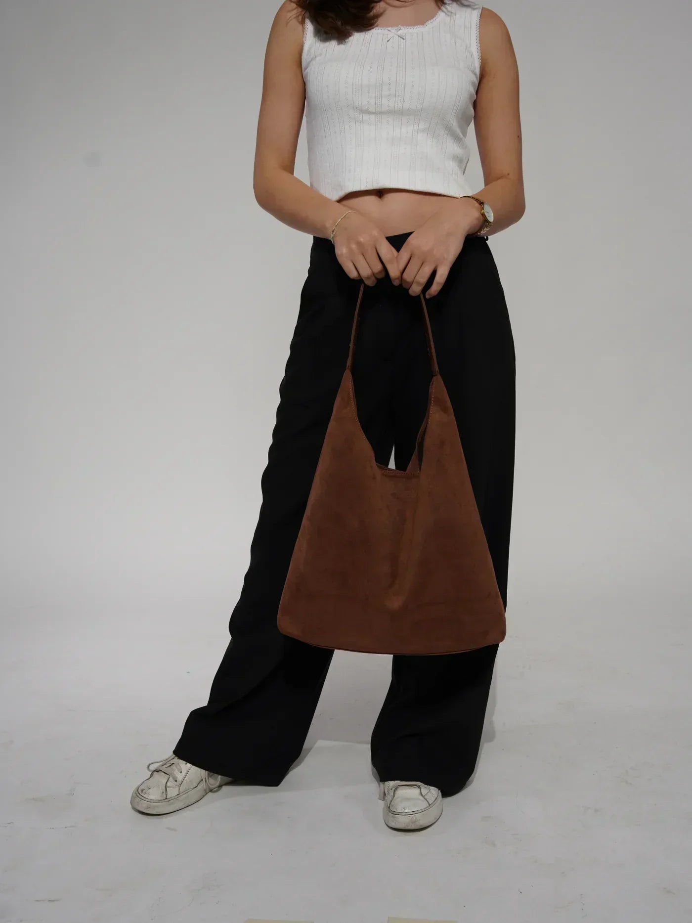 Donna con borsa a spalla marrone in pelle scamosciata, indossa top bianco e pantaloni neri. Moda casual, accessori eleganti, stile minimalista.