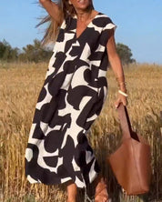 Donna in abito lungo bianco e nero astratto, campo di grano, borsa marrone, estate, moda femminile, stile casual, giornata soleggiata.