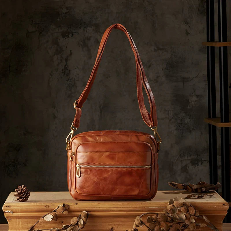 Borsa a tracolla in pelle marrone su sfondo scuro, con cerniere dorate e design elegante. Accessorio moda uomo, stile vintage.