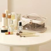 Borsa trasparente per cosmetici su tavolo bianco con trucchi e pennelli; ideale per organizzare prodotti di bellezza e skincare.