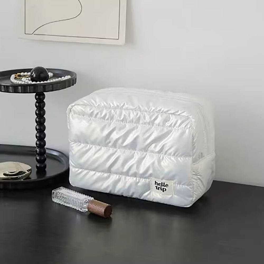Borsa da viaggio bianca trapuntata su tavolo nero, accanto a vassoio con perle e profumo. Design elegante, ideale per organizzare accessori.