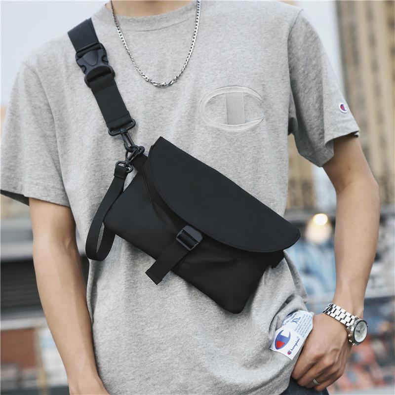 Uomo con borsa a tracolla nera, indossa t-shirt grigia e orologio. Moda casual urbana, accessori maschili, stile streetwear.