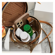 Borsa a tracolla in pelle marrone aperta, contenente smartphone, flaconi cosmetici e accessori. Design elegante, ideale per moda e praticità quotidiana.
