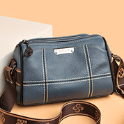 Borsa a tracolla in pelle blu con cuciture bianche, cerniera superiore e tracolla regolabile marrone. Design elegante e moderno per donna.