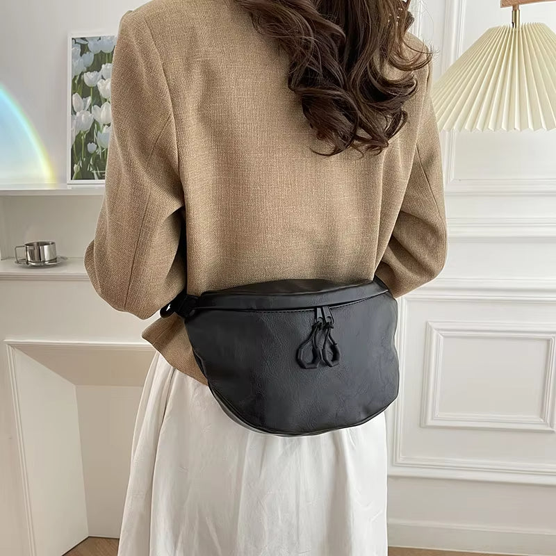 Donna con giacca beige e borsa a tracolla nera in pelle, elegante e moderna, in un ambiente interno minimalista. Accessorio moda femminile.