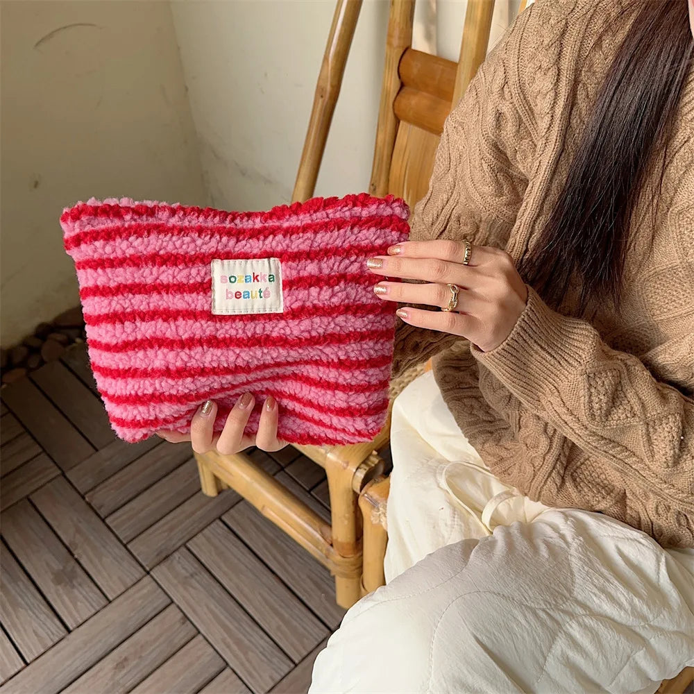 Donna con maglione beige tiene una borsa a righe rosse e bianche in maglia, seduta su sedia di legno. Accessorio moda, stile casual, tendenza autunno.