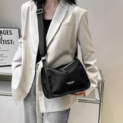 Borsa a tracolla nera in tessuto, indossata su giacca bianca elegante. Design moderno, ideale per moda urbana e casual. Accessorio versatile.