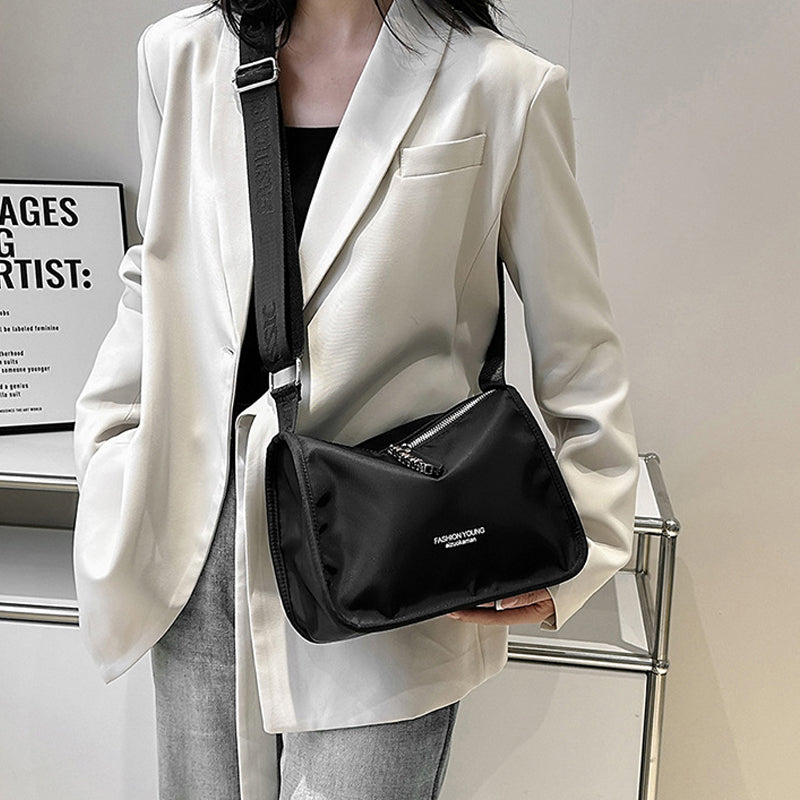 Borsa a tracolla nera in tessuto, indossata su giacca bianca elegante. Design moderno, ideale per moda urbana e casual. Accessorio versatile.