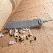 Mocio piatto in microfibra grigia pulisce pavimento in legno, raccogliendo polvere e detriti sotto il divano. Strumento pulizia casa efficiente.